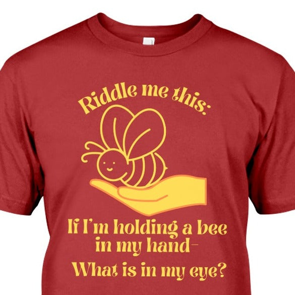 t-shirt with a hand holding a bee and text says Riddle me this:  If I'm holding a bee in my hand..  What is in my eye?