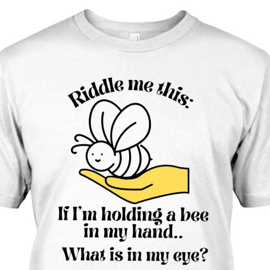 t-shirt with a hand holding a bee and text says Riddle me this: If I'm holding a bee in my hand.. What is in my eye?